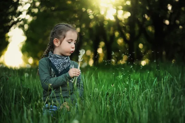 Kind mit Pusteblume im Gegenlicht